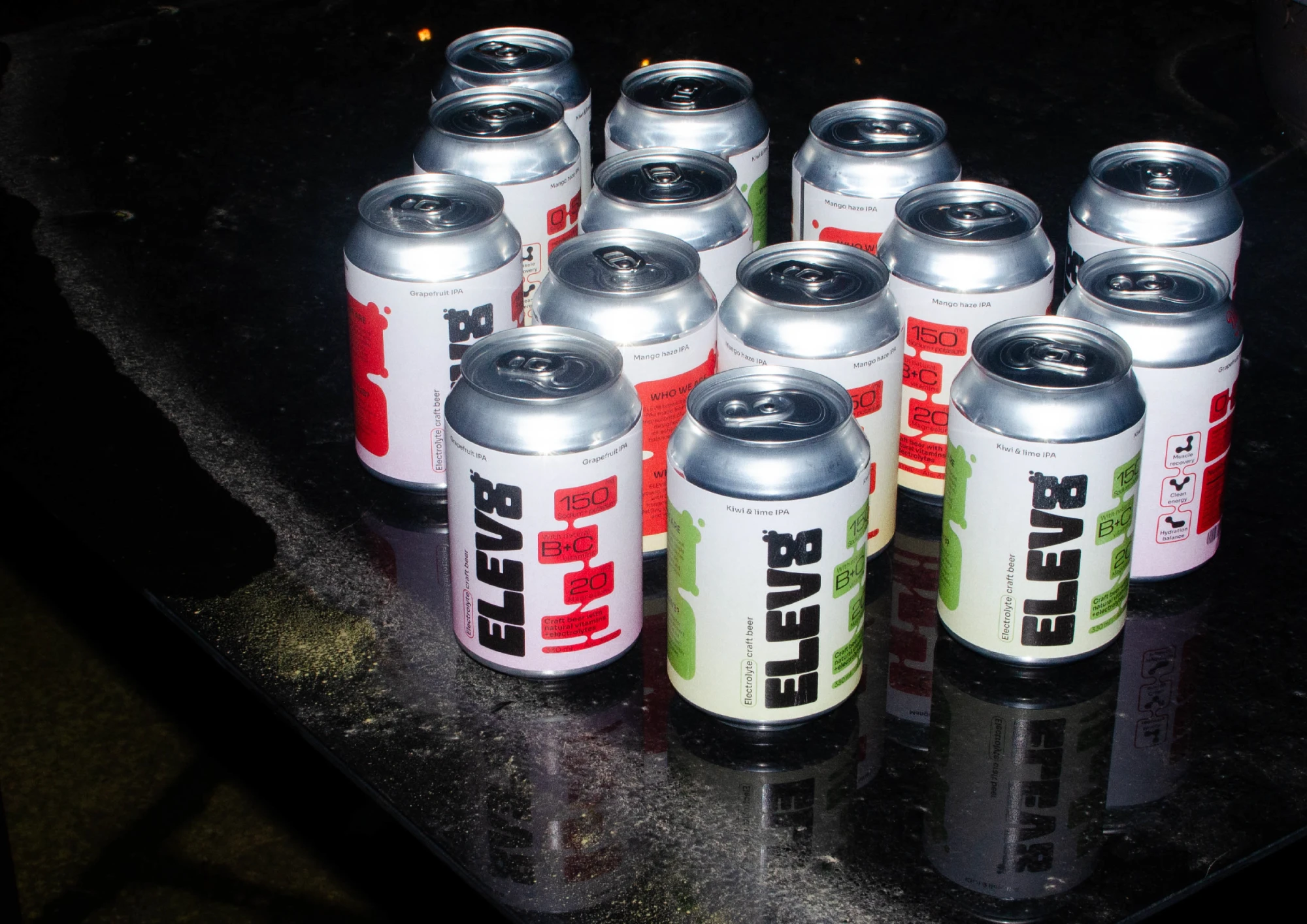 Rows of ELEV8 cans in grapefruit, mango and kiwi flavours on a dark reflective table